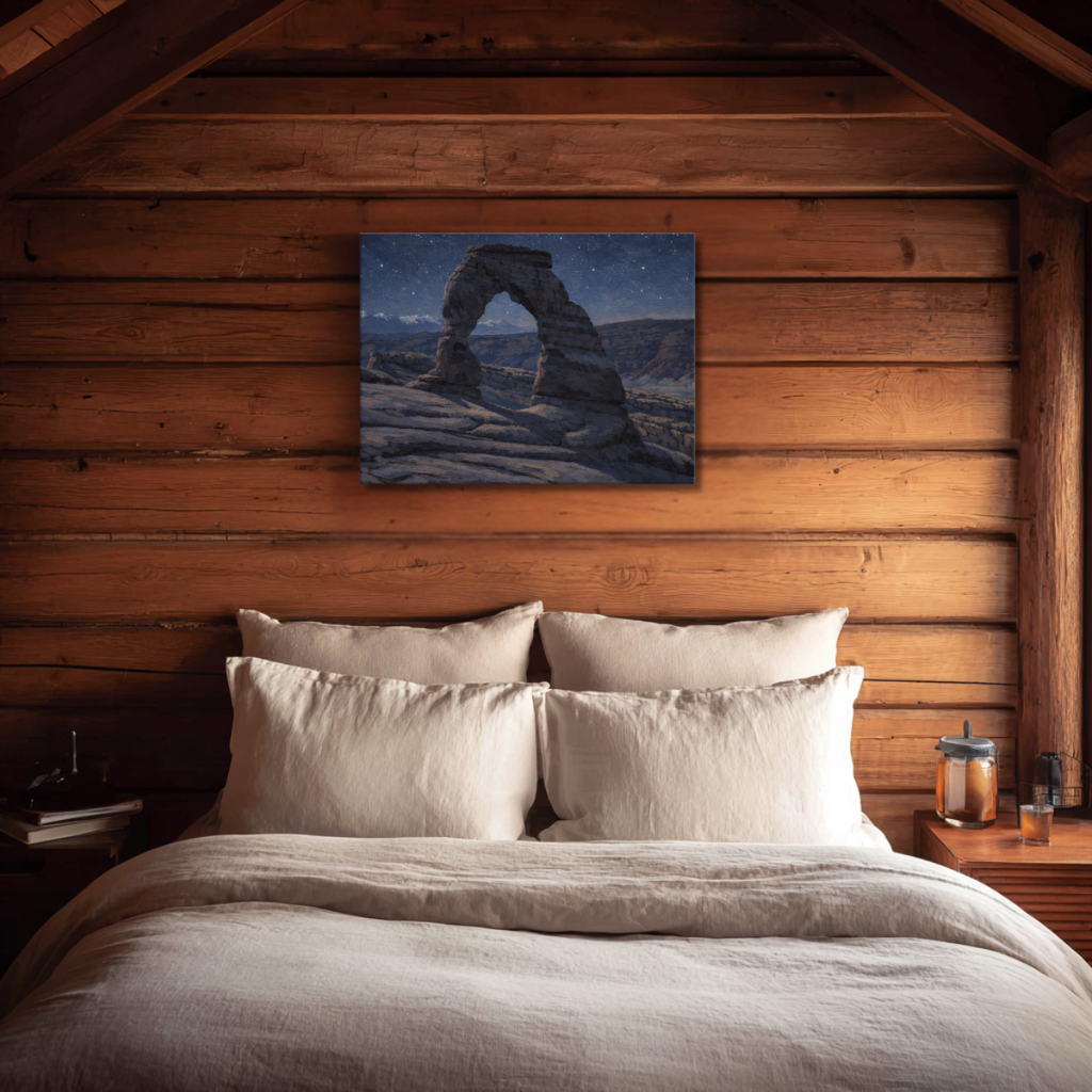 Bedroom with wooden walls, a bed with white bedding, and a painting of a Utah Arch depicted at night, hanging on the wall.